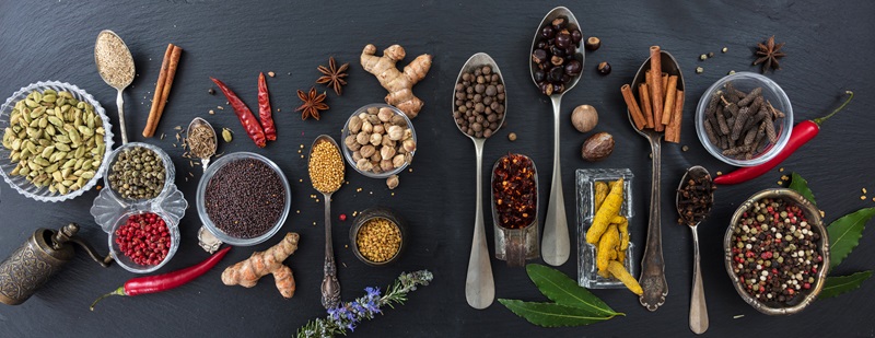 Variety of colorful spices and herbs on black stone background, top view, banner