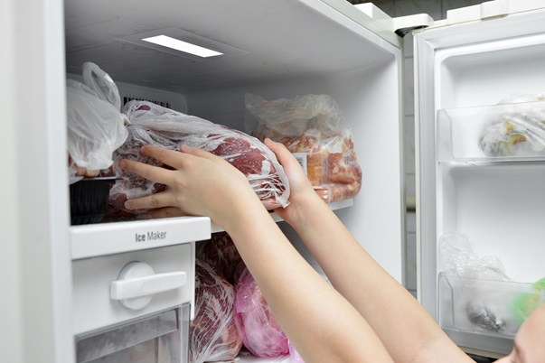The girl takes out a bag of frozen meat from the freezer in the kitchen at home
