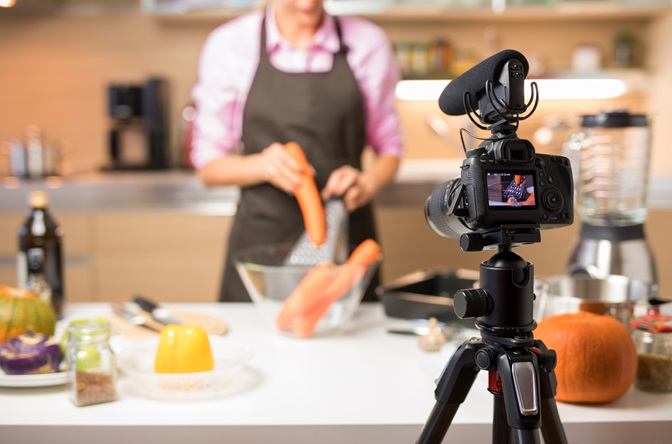 Woman recording video of her cooking for online video blog, focus on camera