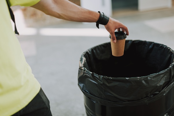 Man throwing paper cup into rubbish bin