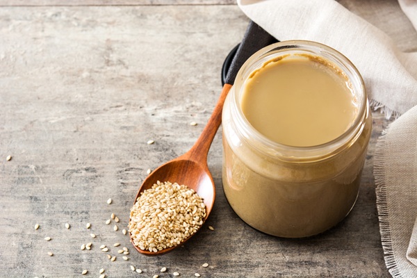 Tahini and sesame seeds on wooden table