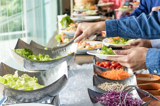 Hands of a young Asian women are selecting salad ingredients at buffet restaurant.